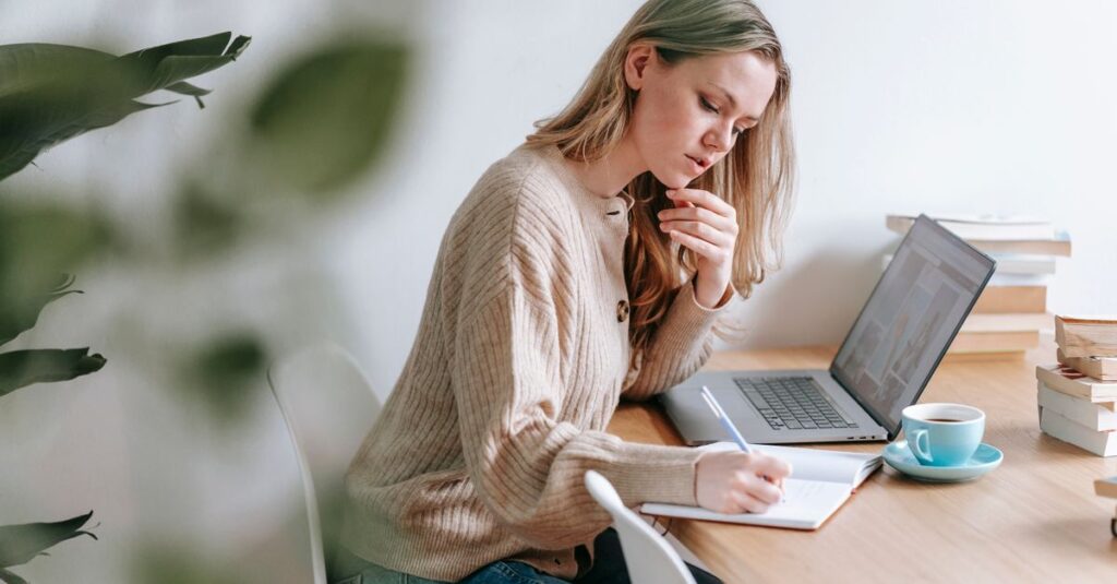 A woman taking notes while working at a laptop